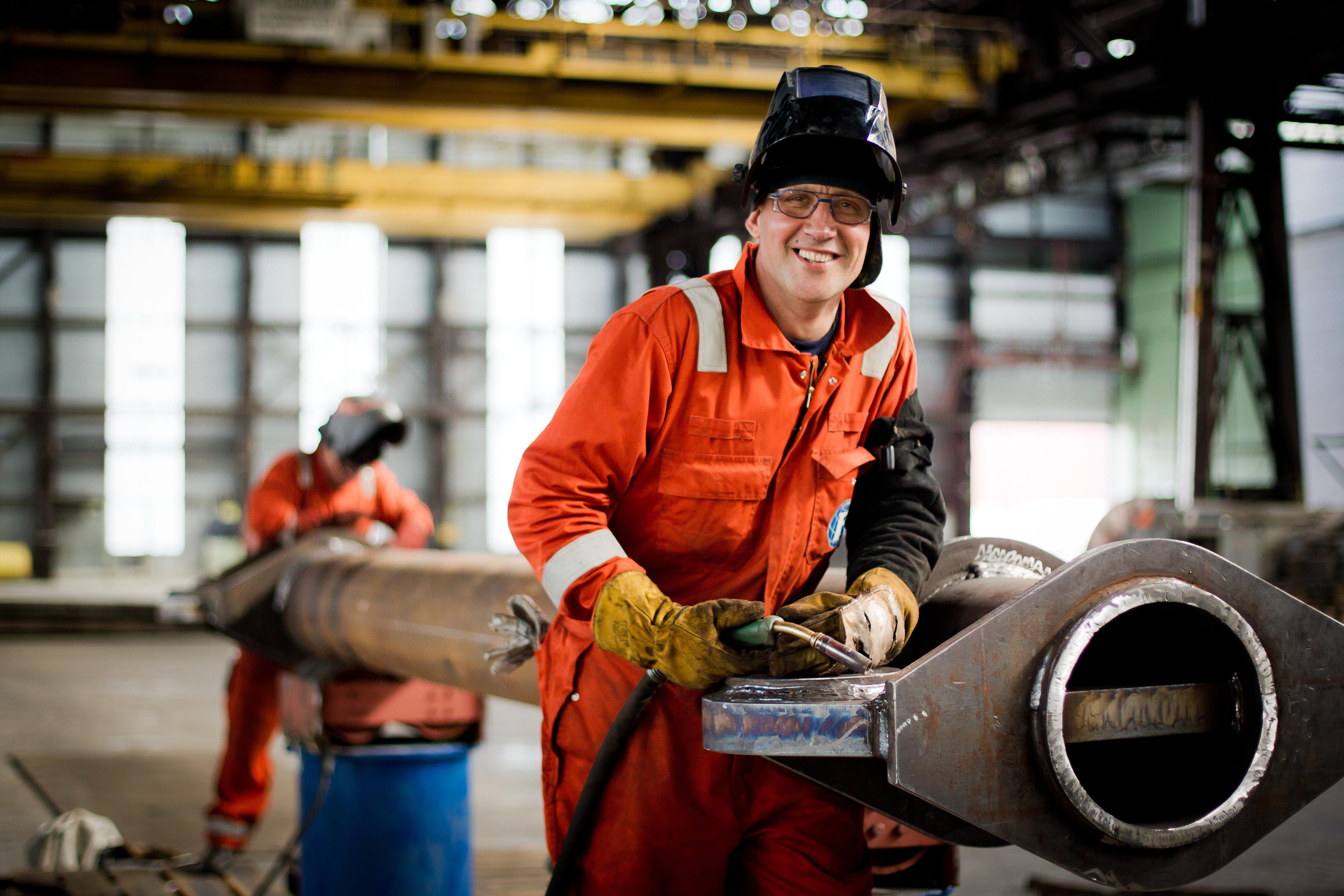 Werknemer in een rode overall en laskap voert laswerkzaamheden uit 